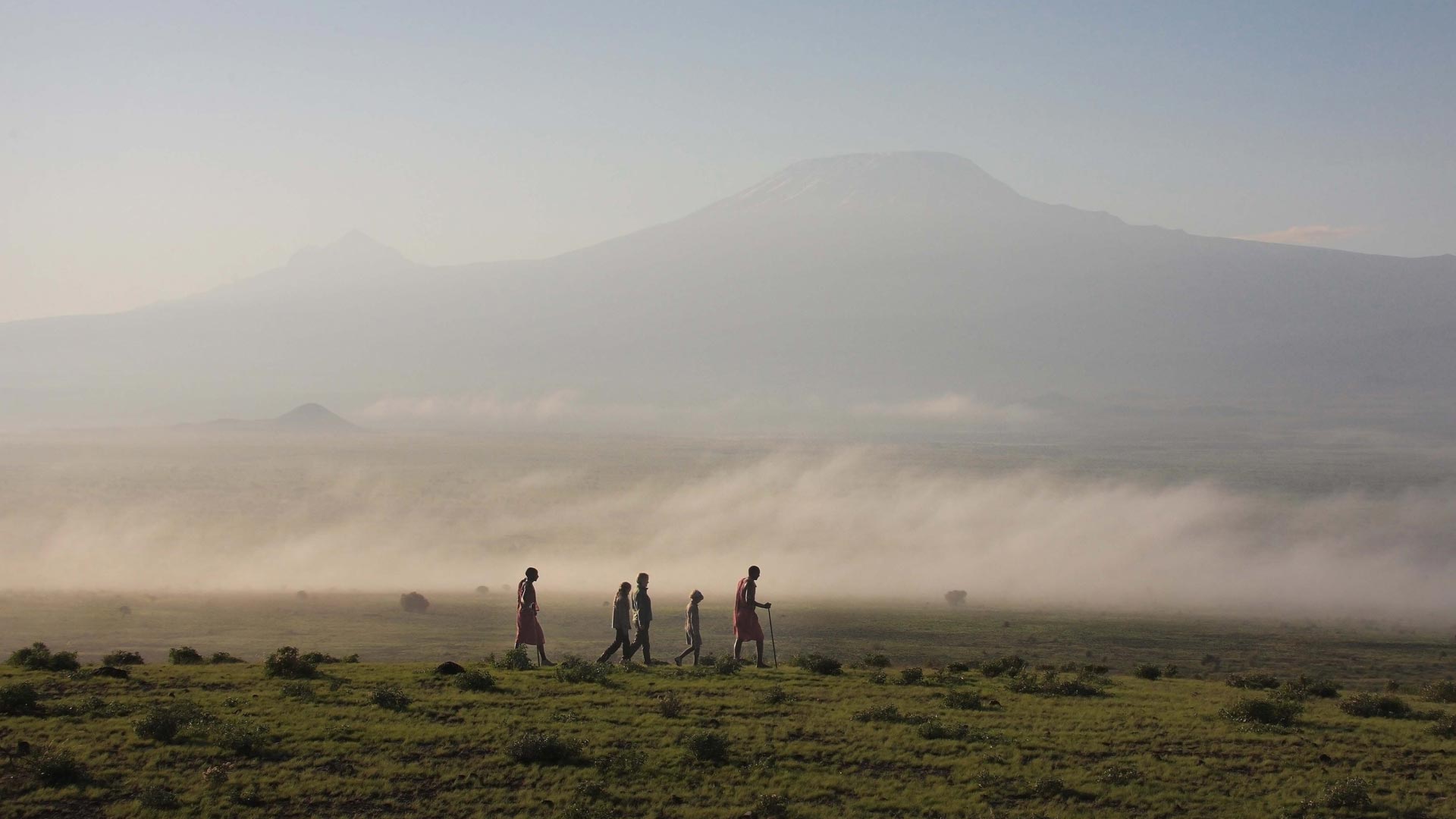 Eine Gruppe Menschen unternimmt eine Wandersafari begleitet von zwei Maasai durch den Amboseli Nationalpark