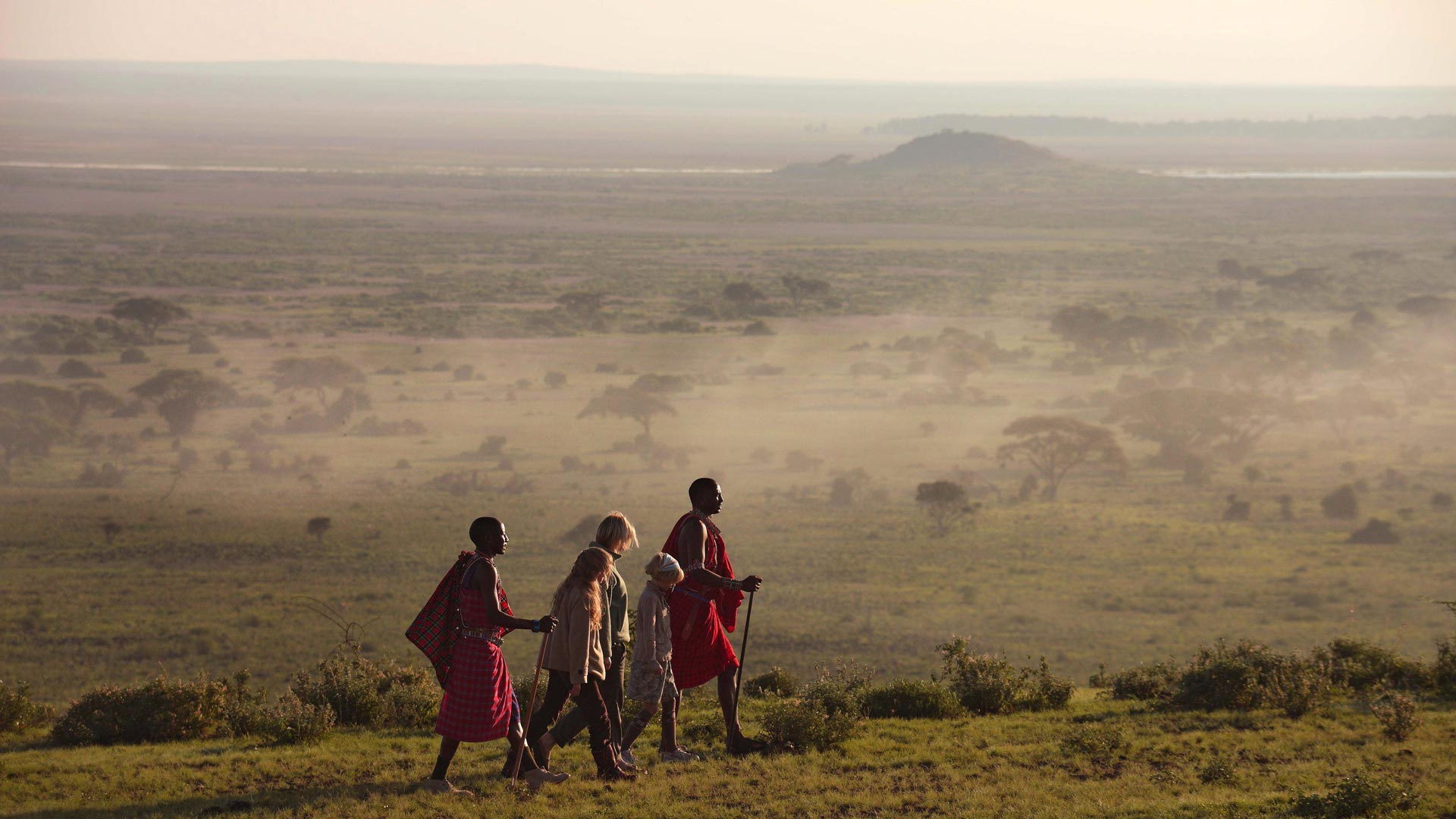 Eine Gruppe Menschen begleitet von zwei Maasai durchstreift den Amboseli Nationalpark während einer Wandersafari